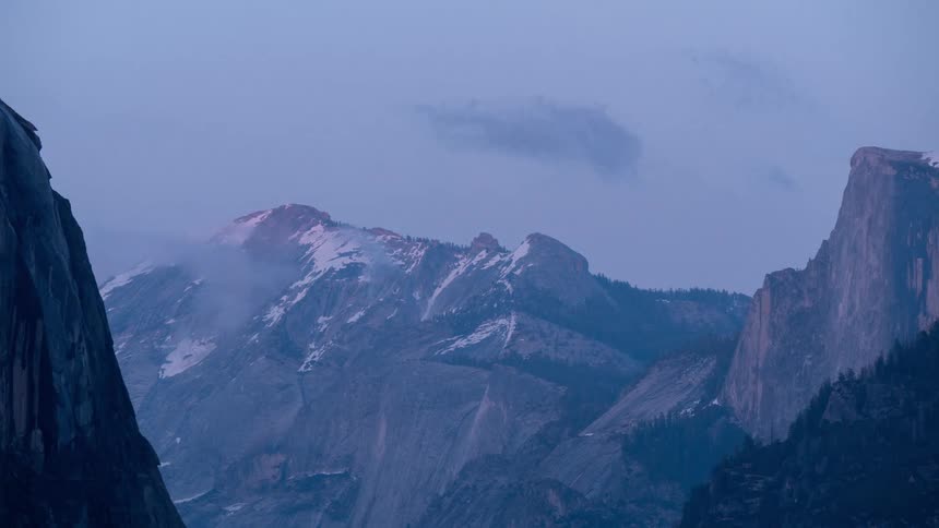 Snow dusted mountains and canyon walls stand under a cloudy twilight sky