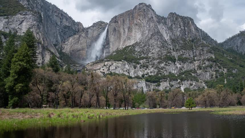 Waterfall cascades down a granite cliff into a forested valley beside a calm river