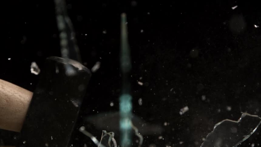 Closeup of a sledgehammer shattering clear glass into fragments in slow motion
