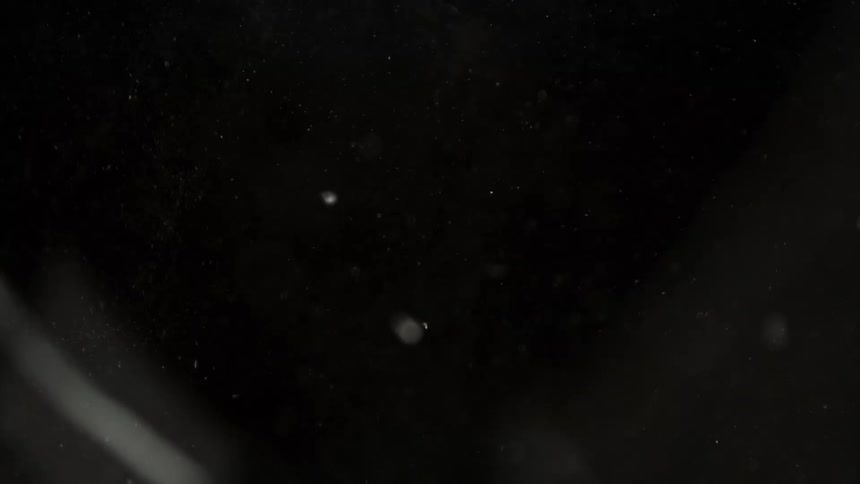 A closeup shot captures shards of glass shattering against a black background