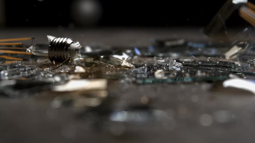 Broken light bulb with shards scattered across dark surface