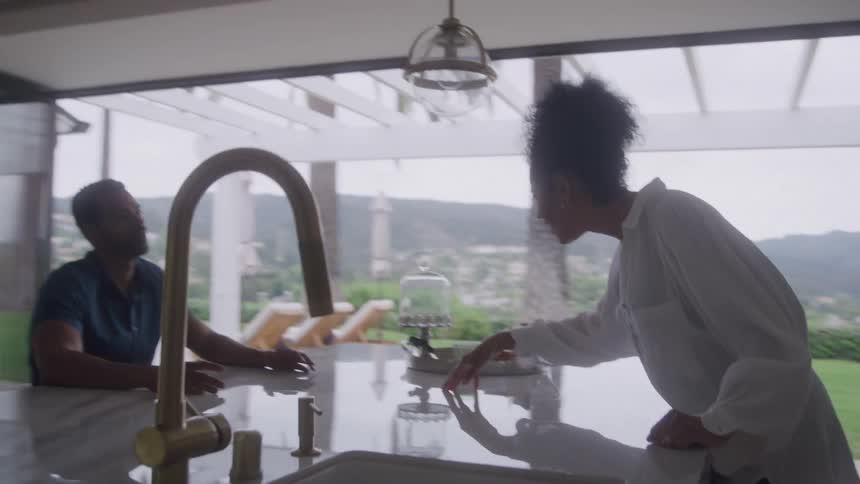 A couple has a serious conversation in their modern kitchen with a beautiful view of their backyard and pool