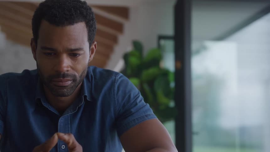 Man crying with head down in indoor setting with plants in the background