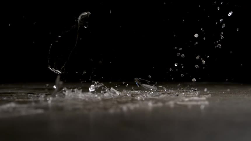 A glass shatters on a dark surface in a dramatic slow motion shot