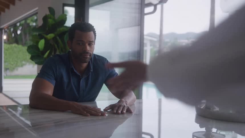 Man seated at marble counter facing windows overlooking pool and green area