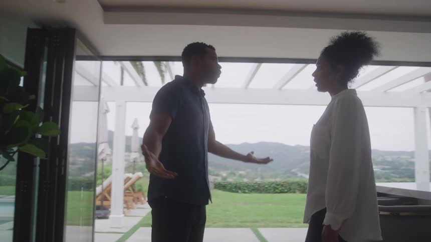 Couple argues inside a modern home with large glass doors and a scenic view