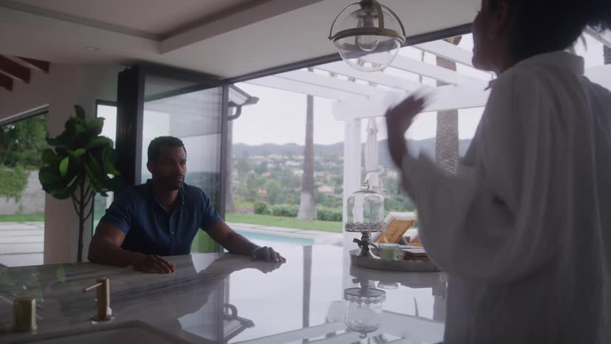 Couple in gestured conversation in modern kitchen with view of wooded outdoor area