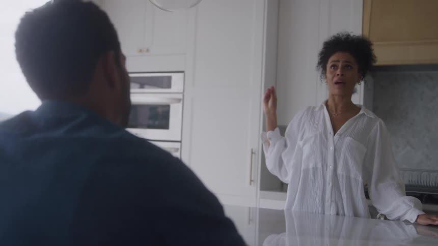 Woman angrily gestures while speaking to a man in a modern kitchen