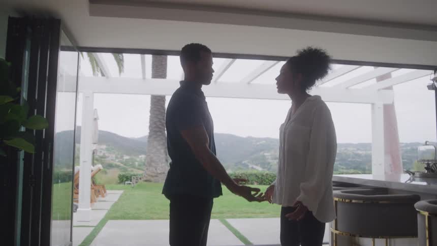 Angry wife yells while husband tries to calm her in a sunlit modern kitchen