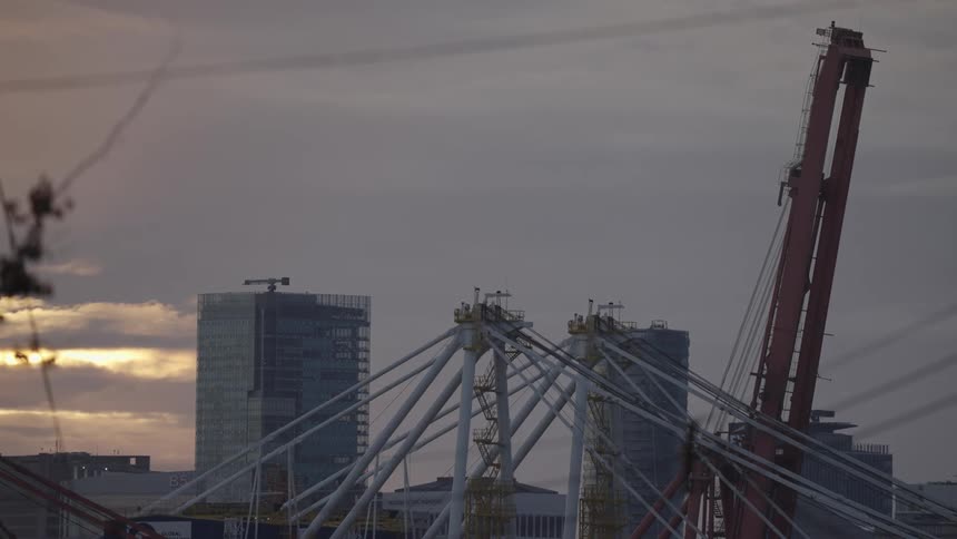Urban construction with cranes and tall buildings at sunset under orange sky