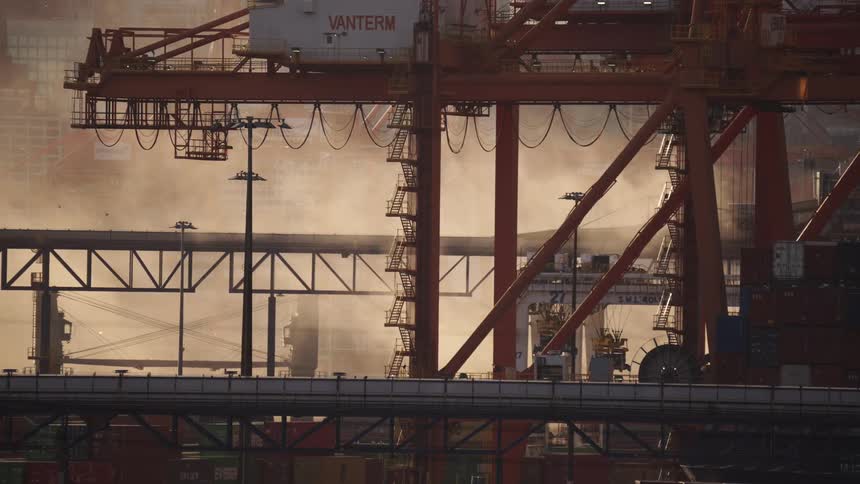 Cranes and containers arranged in port terminal with metal framework and hazy background