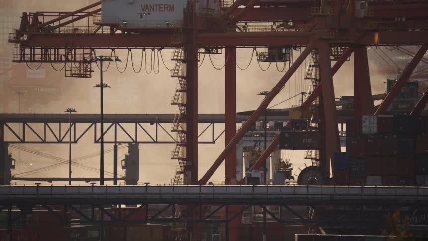 Stacked containers and cranes operating in port terminal with partially visible ship in the background