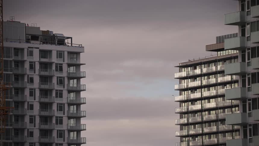 Two modern buildings rise side by side under a cloudy sky