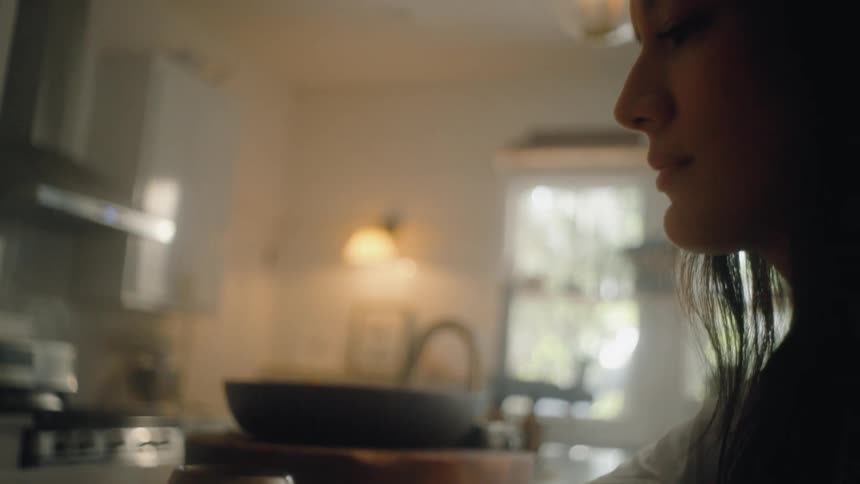 A woman sits at the kitchen counter scrolling on her smartphone