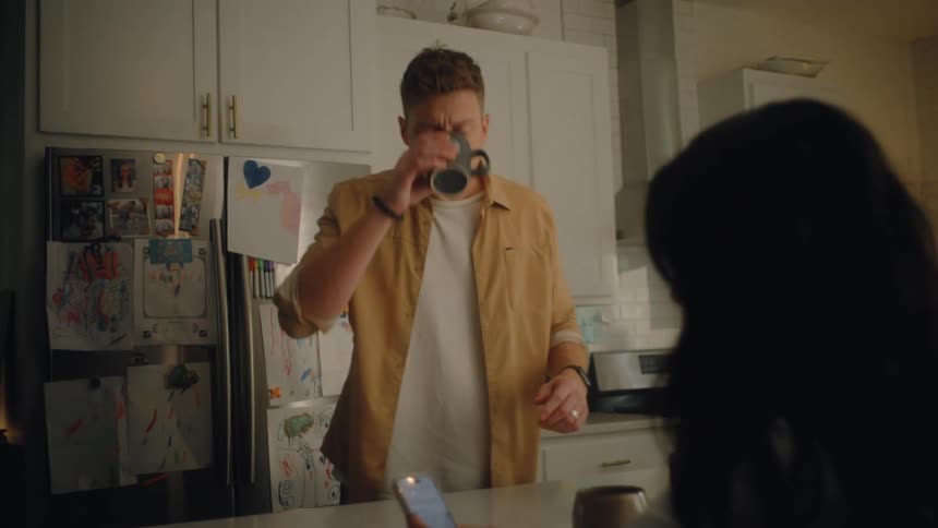 A father son and daughter walk to the dining area where the mother sits using her mobile device the father drinks a cup of coffee while the son and daughter pick up their lunch boxes as they head out for school