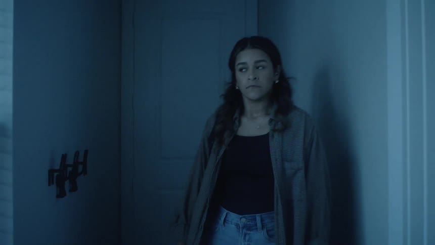 Woman leaning against hallway wall with cautious expression