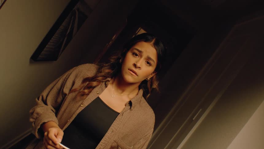Close up of a young woman anxiously checking her pregnancy status with a test strip while standing indoors at night