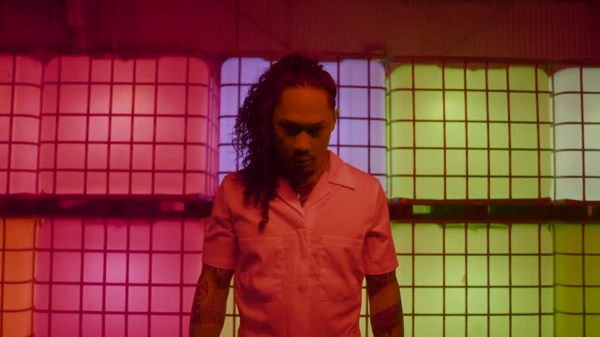 Man with an intense expression stands before panels lit by colorful lights
