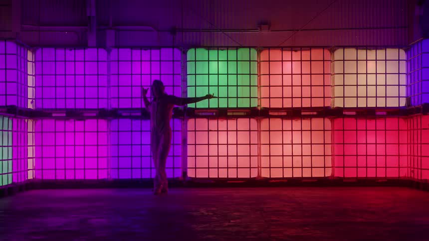A female dancer performs in front of a wall of colorfully illuminated cubes