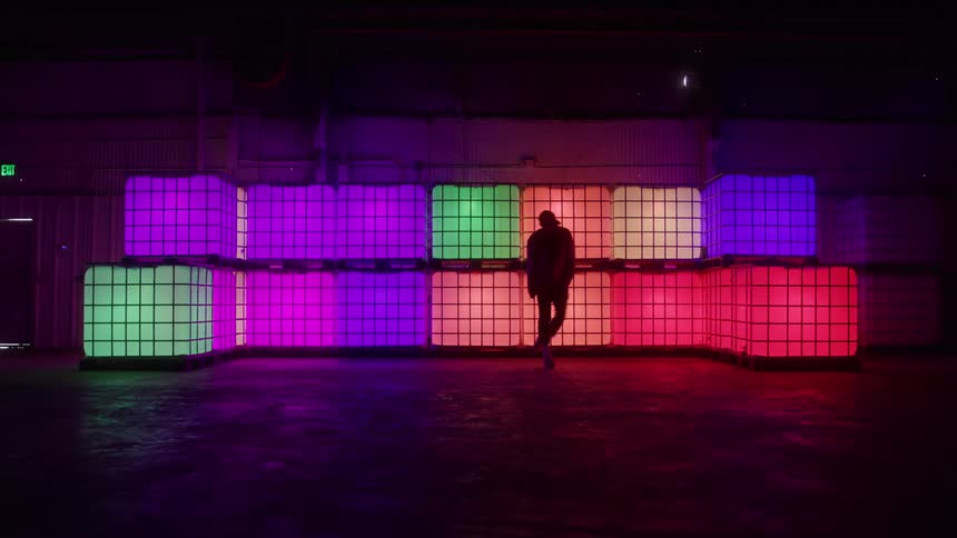 The man is dancing in front of large colorful cubes