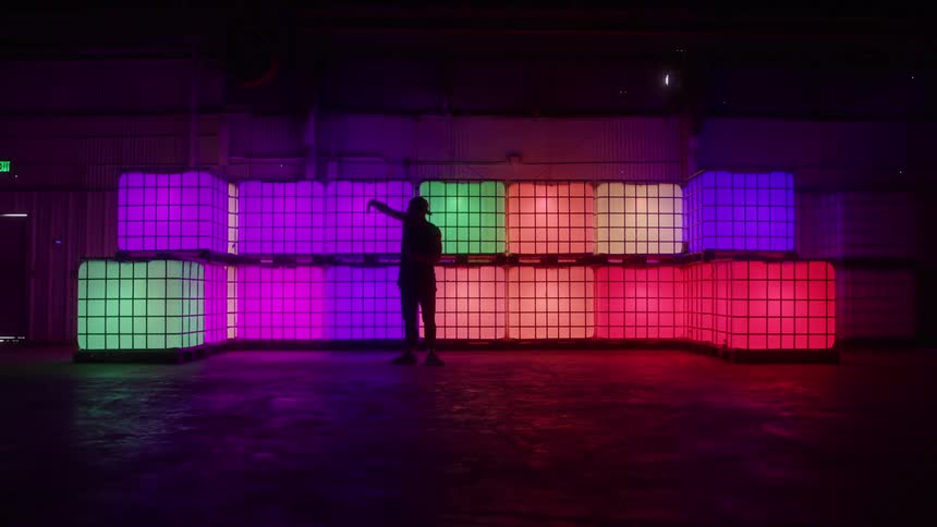 Man dances in front of colorful illuminated cubes in a dark room