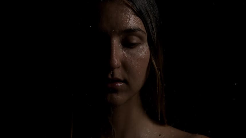 Woman with closed eyes and water droplets running down under soft lighting