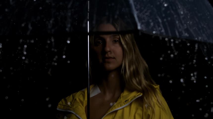 Blonde woman in yellow jacket and open umbrella with rain falling