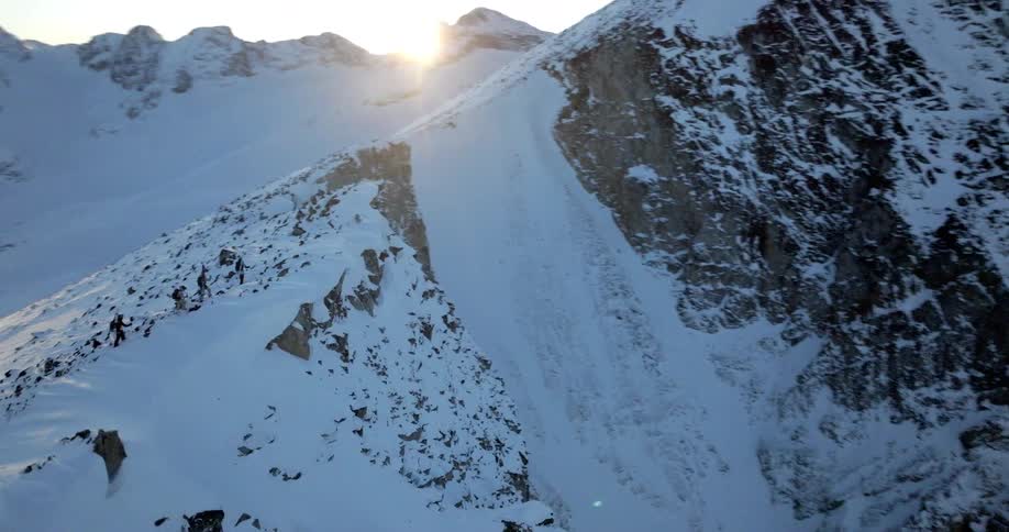 Group of people walking along a snowy mountain cliff
