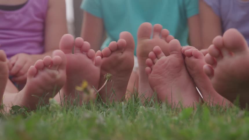 Children sitting on the grass with bare feet stretched forward