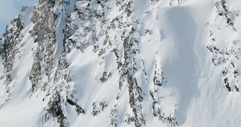 A steep alpine face blanketed in snow with jagged rock spines and a broad windsculpted bowl that looks like an old avalanche path under clear light