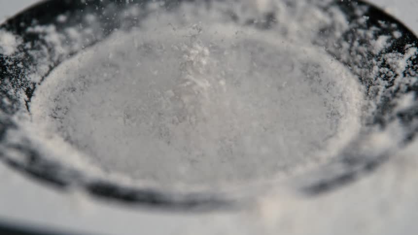The video clip is an extreme closeup of a white powder being dropped or poured into a black object the powder accumulates on the bottom of the vessel which has a distinct circular lip