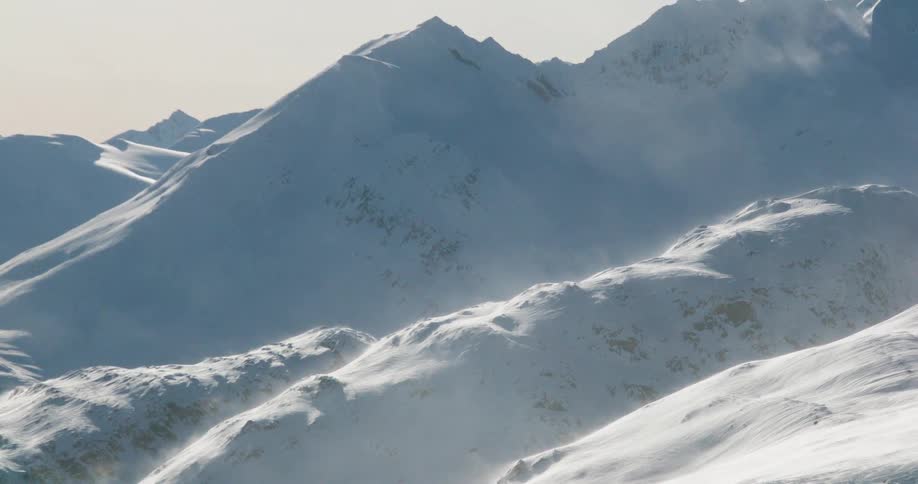 The video clip shows an extreme closeup of a snowcovered jagged mountain range under a soft overcast sky the scene is dominated by the white and grey tones of the peaks and ridges which appear vast and windswept