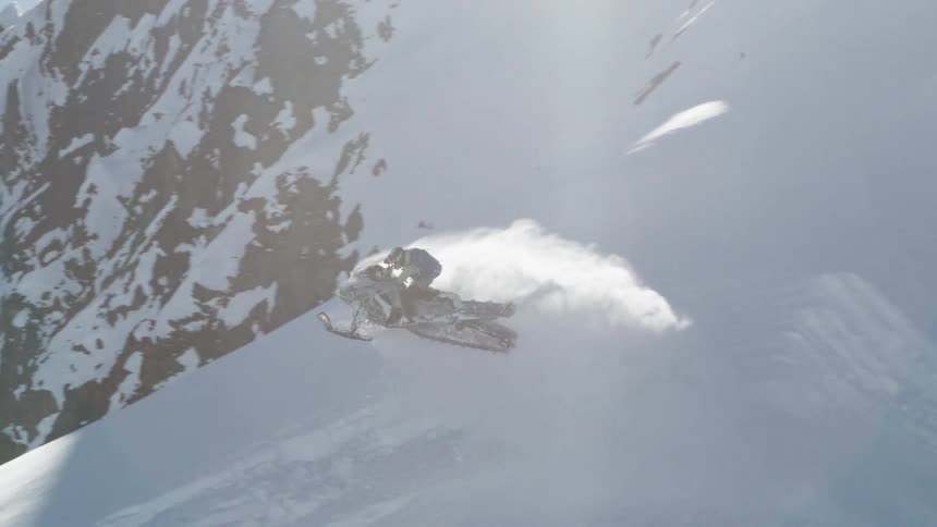Person rides a snowmobile up a steep hill into the air then down the other side on a winter day