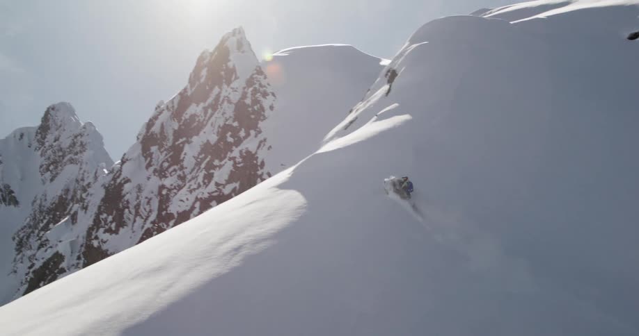A rider on a snowmobile traverse a vast white glacier beneath towering craggy snowcovered cliffs