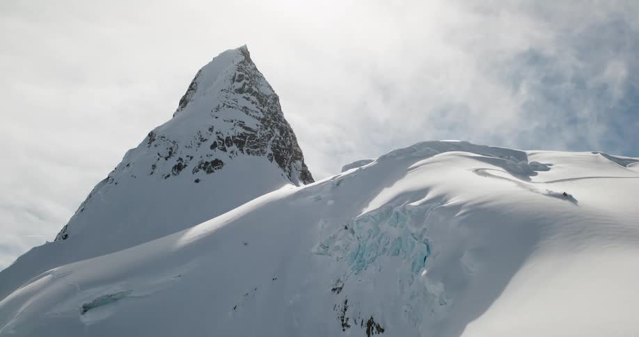 The person rides a snowmobile on the peak of the tall mountain