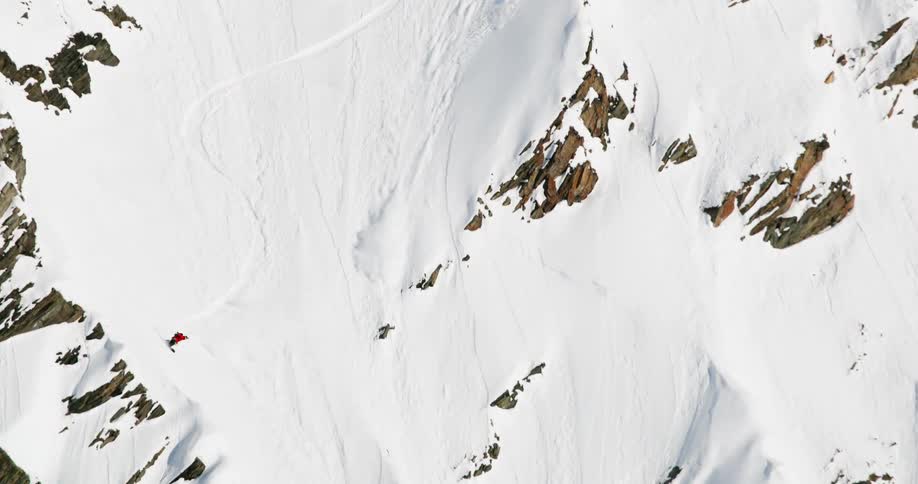 Aerial of a person snowboarding down a mountain slope in an arctic region during daytime