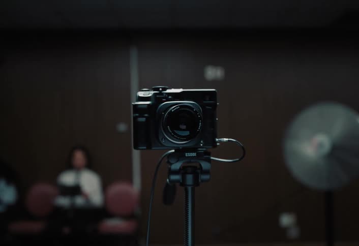 Camera mounted on a tripod in a room with artificial lighting and wooden wall