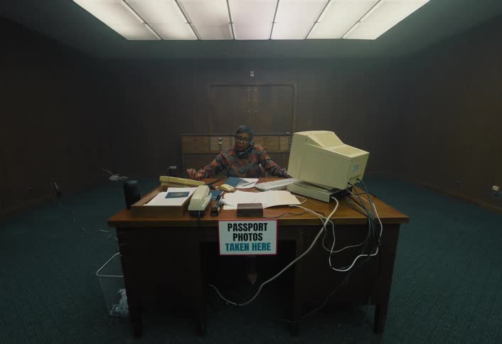 A woman works at a desk while a camera on a tripod is pointed at her