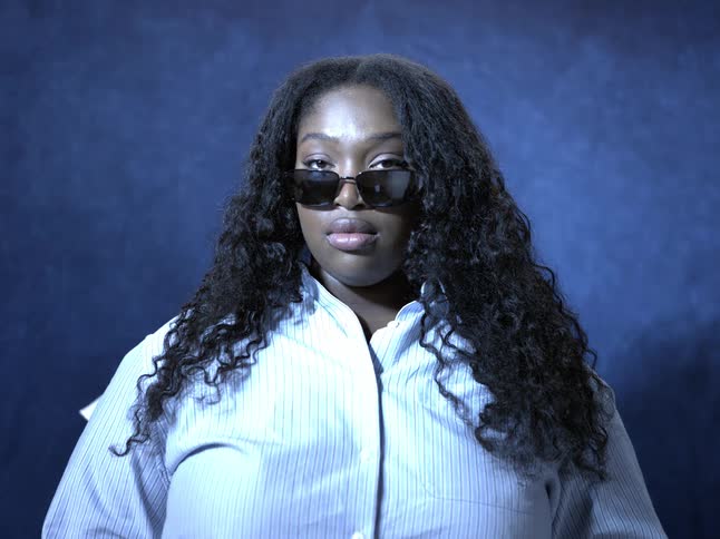 A woman in sunglasses poses confidently against a dark blue background