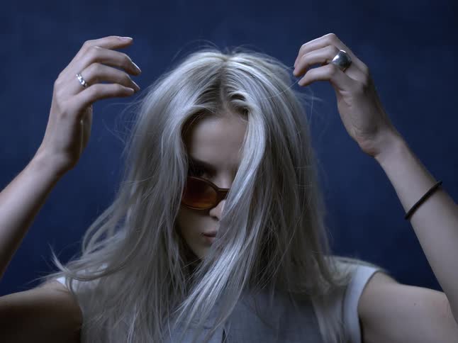 Close up portrait of a young blonde woman arranging her hair during a photo shoot in a studio