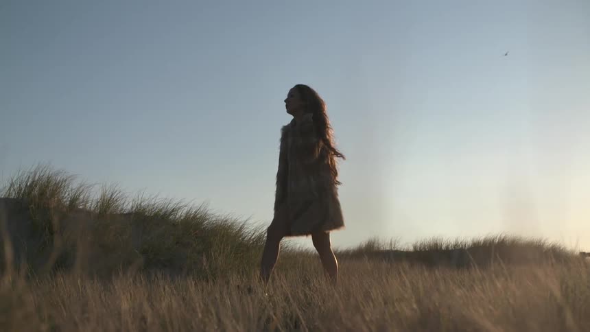 Woman in a fur coat walking through a grassy field