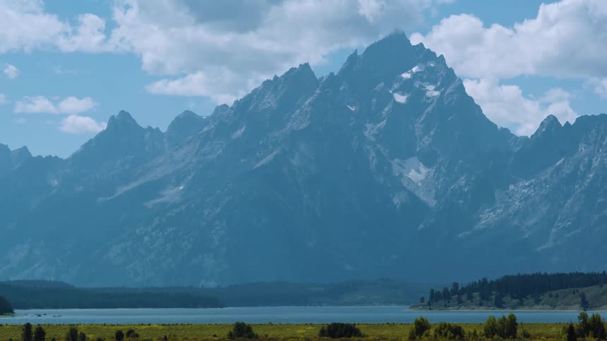 Majestic mountain range rises above a calm lake under a partly cloudy sky