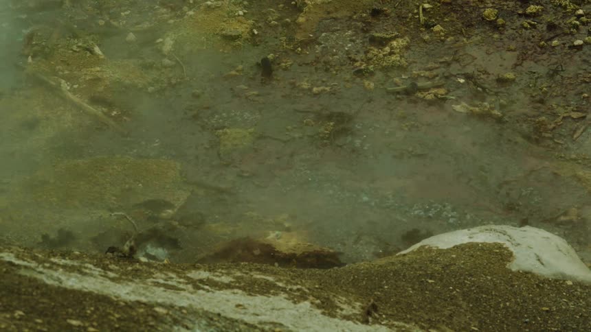 Steam rises from a damp rocky patch of ground with yellowish tones