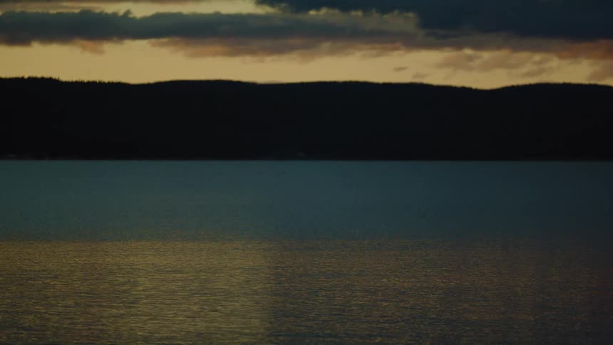 Golden reflection covers calm lake before mountains under orange sky