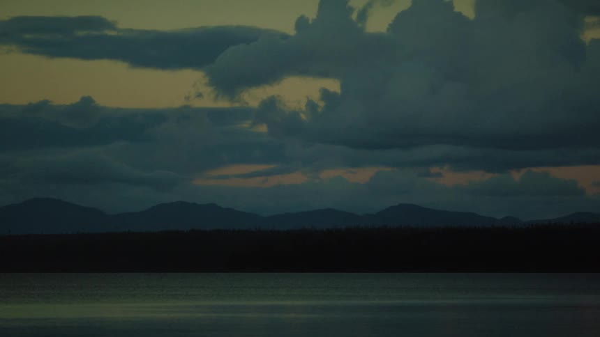 The forest by the lake is covered with darkness at sunrise