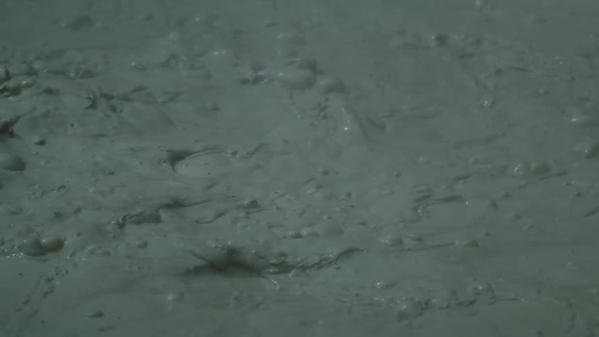 Bubbles form and burst in a thick grayish mud pool