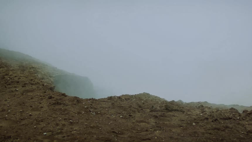 Thick fog rises from the ground obscuring the view of a desolate rocky hillside