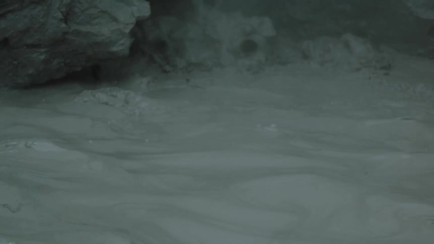 Gray mud pool bubbles near a rocky formation