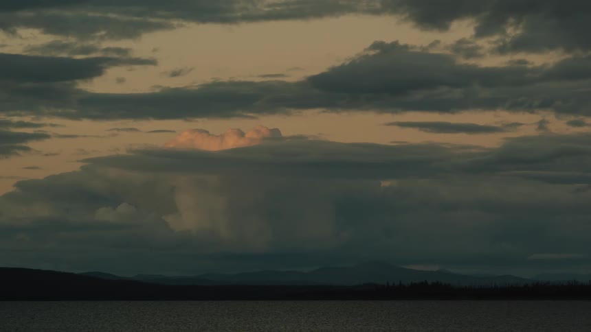 Clouds lit by the sunset above mountains and a calm lake