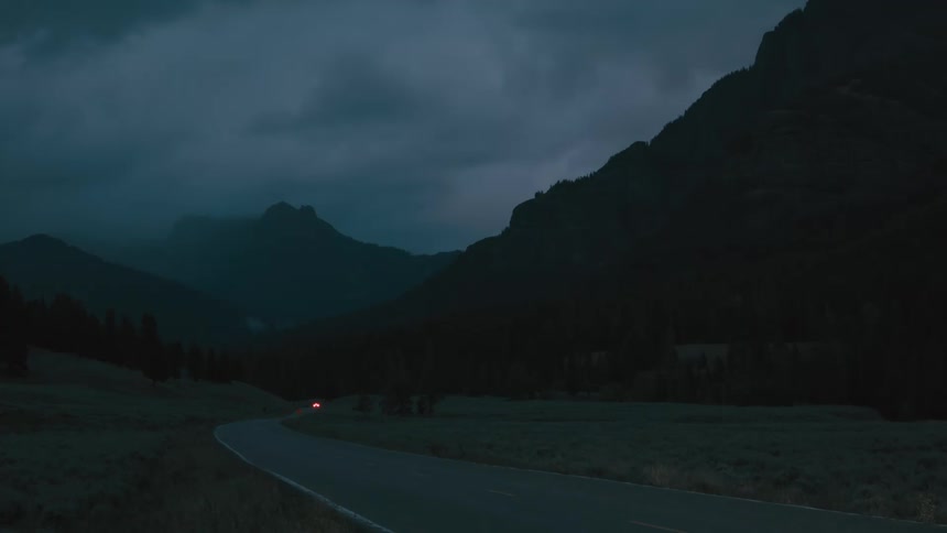 Winding road cuts through a mountainous landscape under the dark evening sky